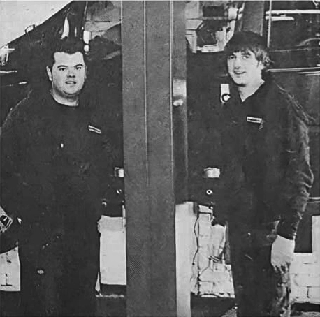 Two mechanics standing in an early workshop.